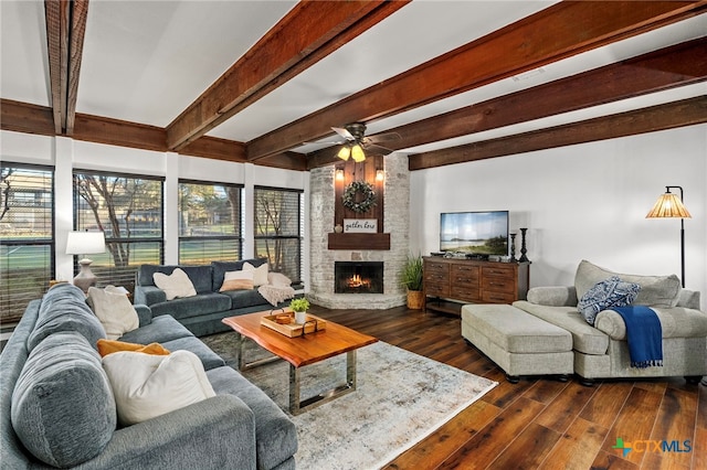 living area with dark wood-type flooring, beam ceiling, a stone fireplace, and a ceiling fan