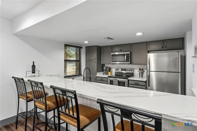 kitchen featuring appliances with stainless steel finishes, dark wood-style flooring, a peninsula, and a kitchen bar