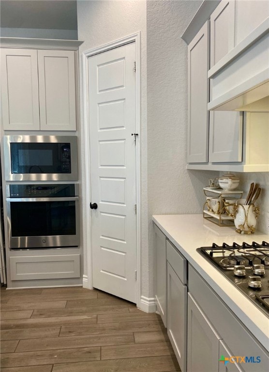 429 Juana Way, New Braunfels, TX 78132 - kitchen featuring stainless steel appliances, light wood-style floors, a textured wall, exhaust hood, and light countertops