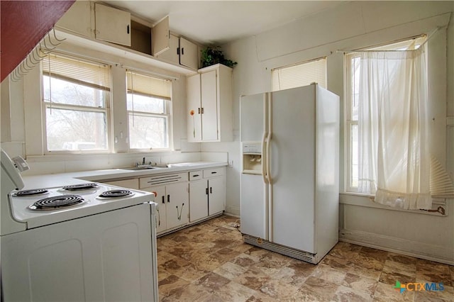 kitchen with white appliances, baseboards, white cabinets, light countertops, and a sink