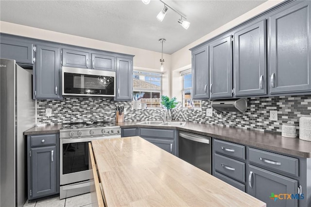 kitchen featuring light tile patterned floors, tasteful backsplash, appliances with stainless steel finishes, pendant lighting, and a sink