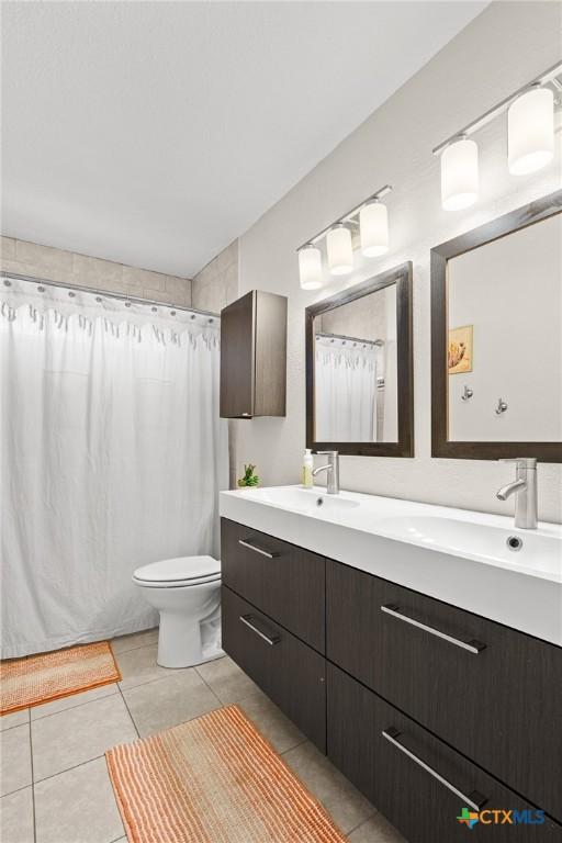 full bath featuring toilet, double vanity, a sink, and tile patterned floors