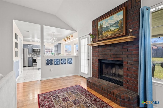 living room featuring light wood-type flooring, a fireplace, and vaulted ceiling