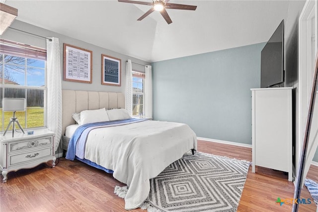 bedroom with vaulted ceiling, ceiling fan, light wood-style flooring, and baseboards