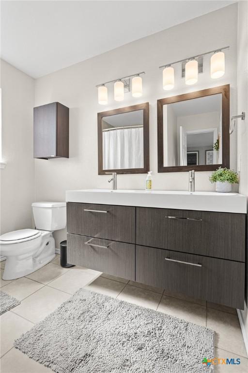 full bath with toilet, tile patterned flooring, double vanity, and a sink