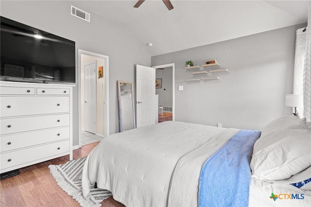 bedroom featuring a ceiling fan, visible vents, vaulted ceiling, and wood finished floors