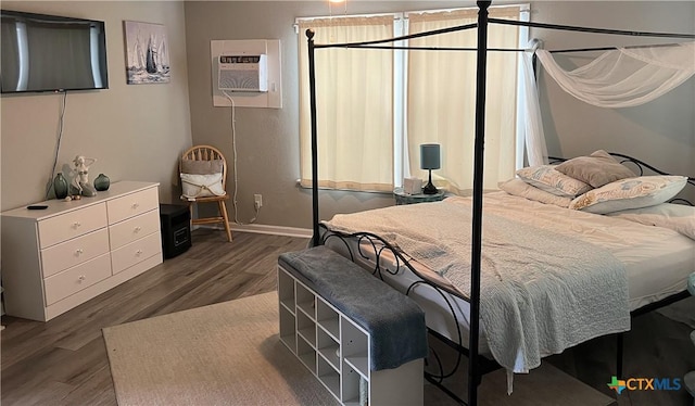 bedroom with a wall unit AC, baseboards, and wood finished floors