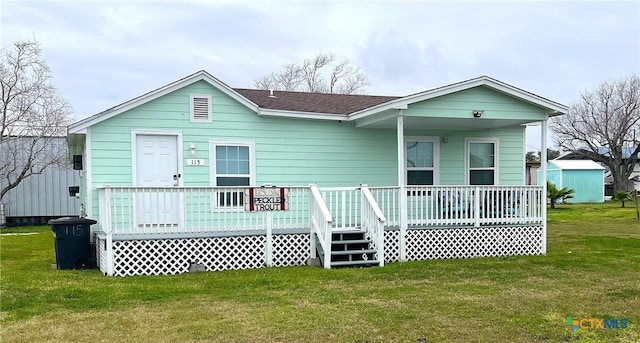 view of front facade with a shingled roof, a front yard, and covered porch