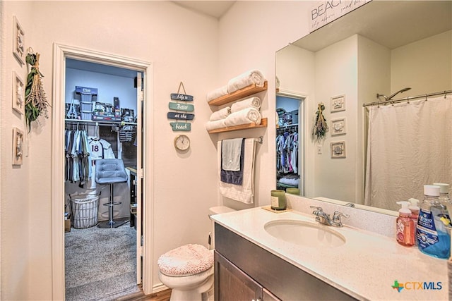 full bath with a spacious closet, vanity, wood finished floors, and toilet