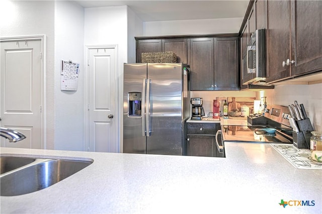kitchen featuring appliances with stainless steel finishes, a sink, dark brown cabinetry, and light countertops