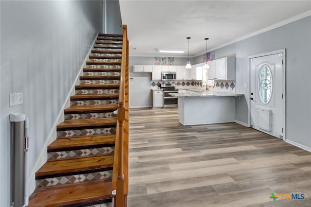 kitchen with white cabinets, ornamental molding, appliances with stainless steel finishes, light stone counters, and pendant lighting