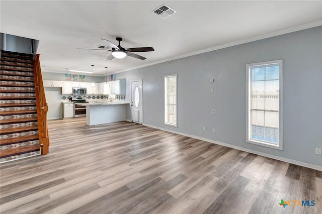 unfurnished living room with crown molding, light wood finished floors, visible vents, a ceiling fan, and stairs