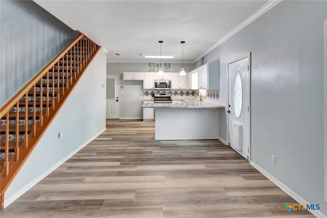 kitchen with appliances with stainless steel finishes, ornamental molding, white cabinetry, light stone countertops, and a peninsula