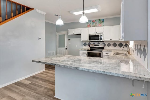 kitchen with a peninsula, a sink, white cabinetry, hanging light fixtures, and appliances with stainless steel finishes