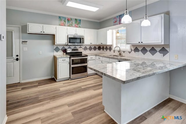 kitchen with a peninsula, a sink, white cabinets, appliances with stainless steel finishes, and pendant lighting