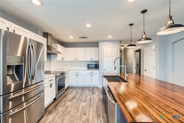 10122 Divine Breeze, San Antonio, TX 78251 - kitchen featuring stainless steel appliances, butcher block countertops, wall chimney exhaust hood, white cabinetry, and recessed lighting