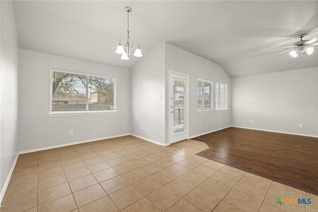 empty room featuring lofted ceiling, wood finished floors, a wealth of natural light, and ceiling fan with notable chandelier