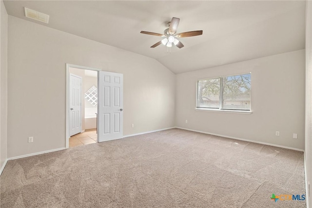 unfurnished bedroom with lofted ceiling, light carpet, visible vents, baseboards, and ensuite bath