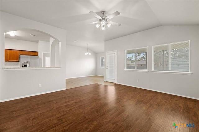 unfurnished living room with vaulted ceiling, ceiling fan, arched walkways, and wood finished floors