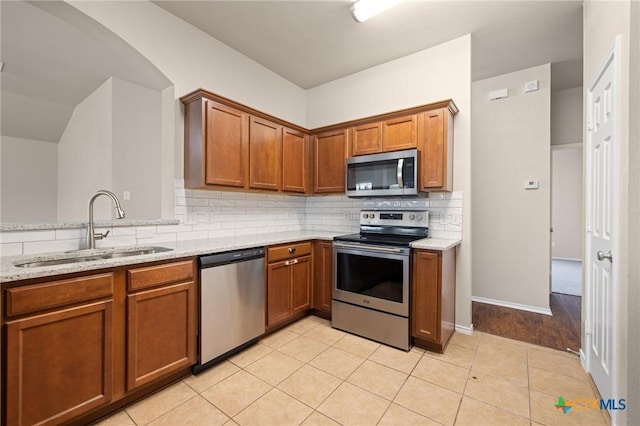 kitchen featuring brown cabinets, tasteful backsplash, appliances with stainless steel finishes, a sink, and light stone countertops