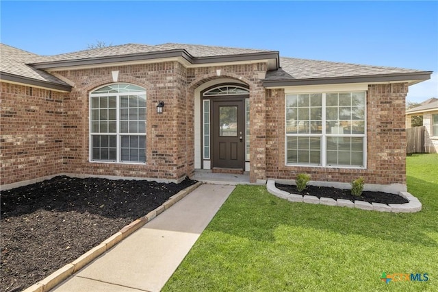 property entrance with brick siding, a shingled roof, and a yard