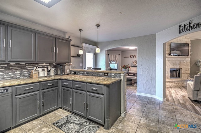 kitchen featuring a stone fireplace, kitchen peninsula, hanging light fixtures, and a textured ceiling