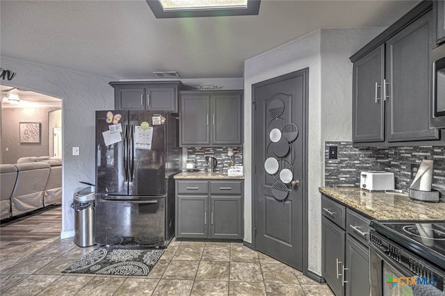 kitchen with dark stone counters, gray cabinets, appliances with stainless steel finishes, and tasteful backsplash