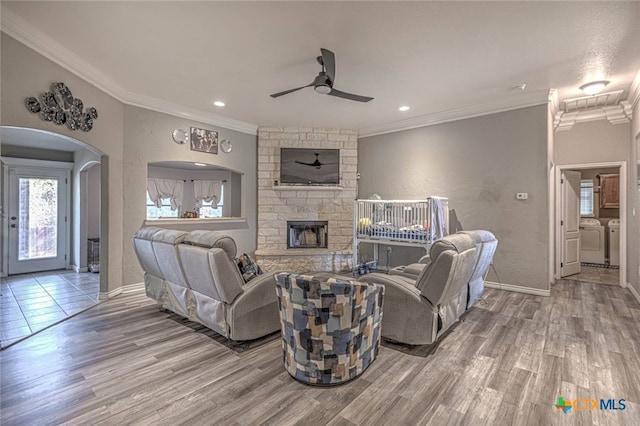 living room with wood-type flooring, ornamental molding, a fireplace, washer and dryer, and ceiling fan