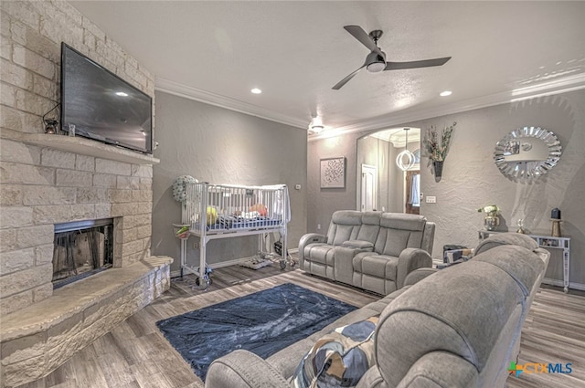 living room featuring a stone fireplace, ceiling fan, wood-type flooring, and ornamental molding