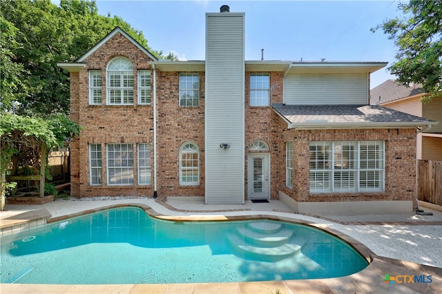 back of property with brick siding, a chimney, a patio area, fence, and an outdoor pool