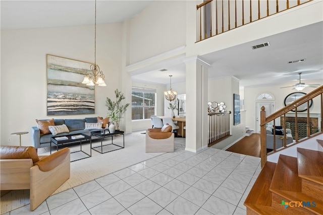 living area with stairs, visible vents, a high ceiling, ornate columns, and ceiling fan with notable chandelier