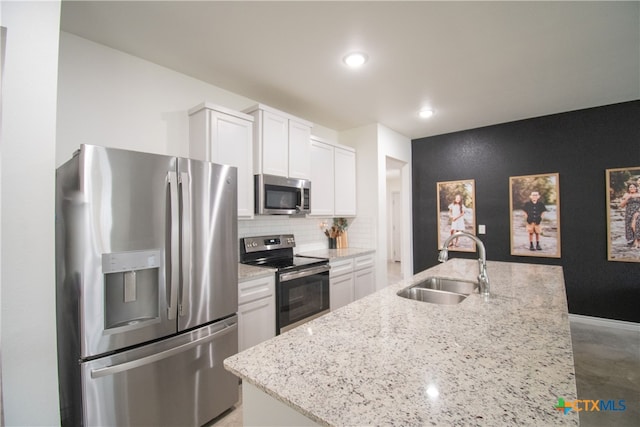 kitchen with tasteful backsplash, stainless steel appliances, light stone countertops, sink, and white cabinets