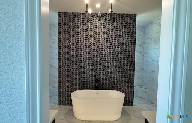 full bathroom featuring marble finish floor, a freestanding bath, and stone wall