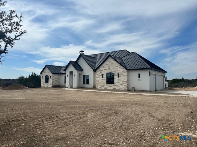 view of front of house with concrete driveway, stone siding, metal roof, an attached garage, and a standing seam roof