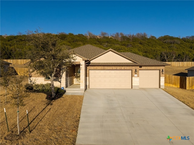 single story home with a garage, a shingled roof, brick siding, fence, and concrete driveway