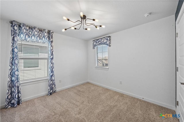 carpeted spare room with baseboards and an inviting chandelier