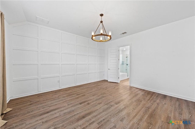 spare room with vaulted ceiling, a chandelier, visible vents, a decorative wall, and wood finished floors