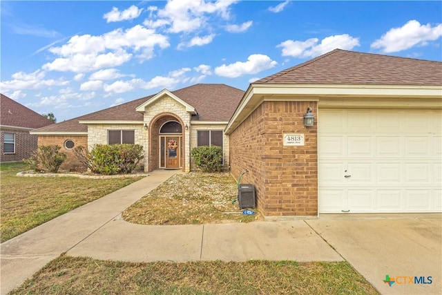 ranch-style home with an attached garage, a shingled roof, a front yard, and brick siding