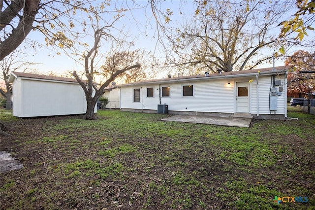 back house at dusk with a yard, central AC, and a patio area