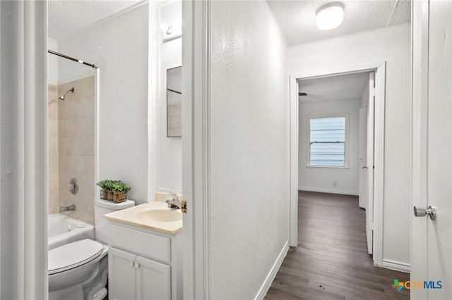 full bathroom with vanity, hardwood / wood-style flooring, tiled shower / bath combo, toilet, and a textured ceiling