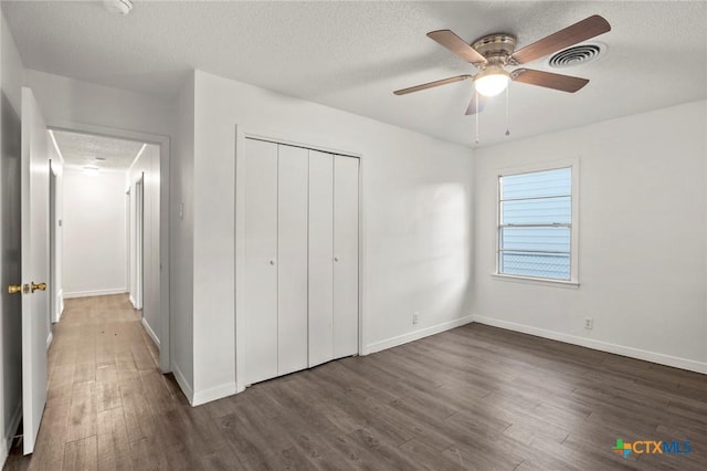 unfurnished bedroom with a textured ceiling, dark hardwood / wood-style flooring, a closet, and ceiling fan