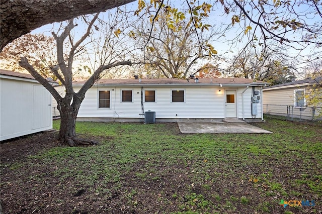 back house at dusk with a lawn, a patio, and central AC unit