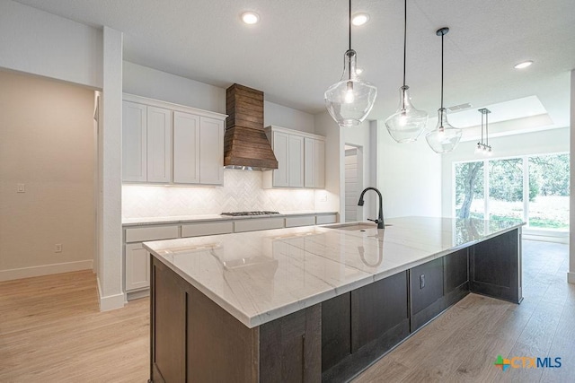 kitchen with a sink, custom range hood, light wood-style flooring, white cabinets, and recessed lighting