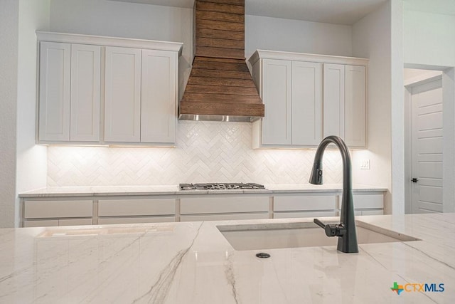 kitchen featuring tasteful backsplash, gas stovetop, a sink, premium range hood, and light stone counters