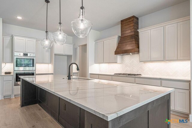 kitchen featuring a sink, custom range hood, appliances with stainless steel finishes, a spacious island, and tasteful backsplash