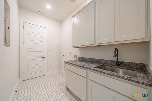 kitchen with a sink, baseboards, dark stone counters, white cabinetry, and electric panel
