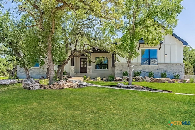 view of front facade with stone siding, a front yard, and board and batten siding