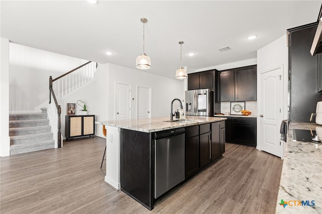 427 Bluejack Way, Hutto, TX 78634 - kitchen featuring stainless steel appliances, a sink, light wood-style floors, an island with sink, and light stone counters