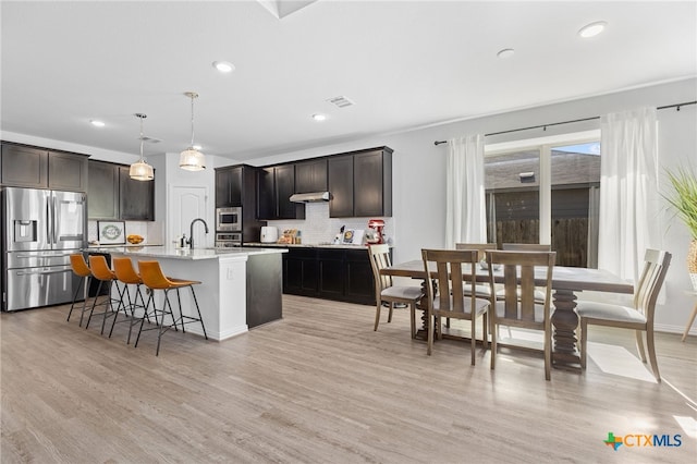 427 Bluejack Way, Hutto, TX 78634 - kitchen featuring appliances with stainless steel finishes, backsplash, a kitchen island with sink, a breakfast bar, and light wood-type flooring