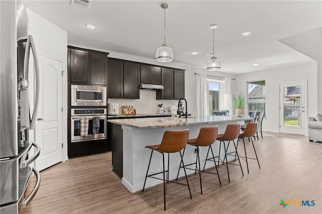 427 Bluejack Way, Hutto, TX 78634 - kitchen with appliances with stainless steel finishes, a kitchen bar, backsplash, light wood-type flooring, and recessed lighting